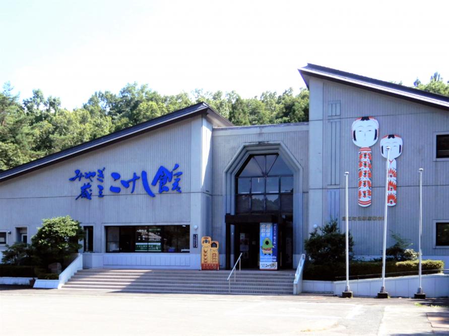蔵王町「みやぎ蔵王こけし館」の外観と、入り口横の壁面に飾られた巨大な伝統こけしのオブジェ